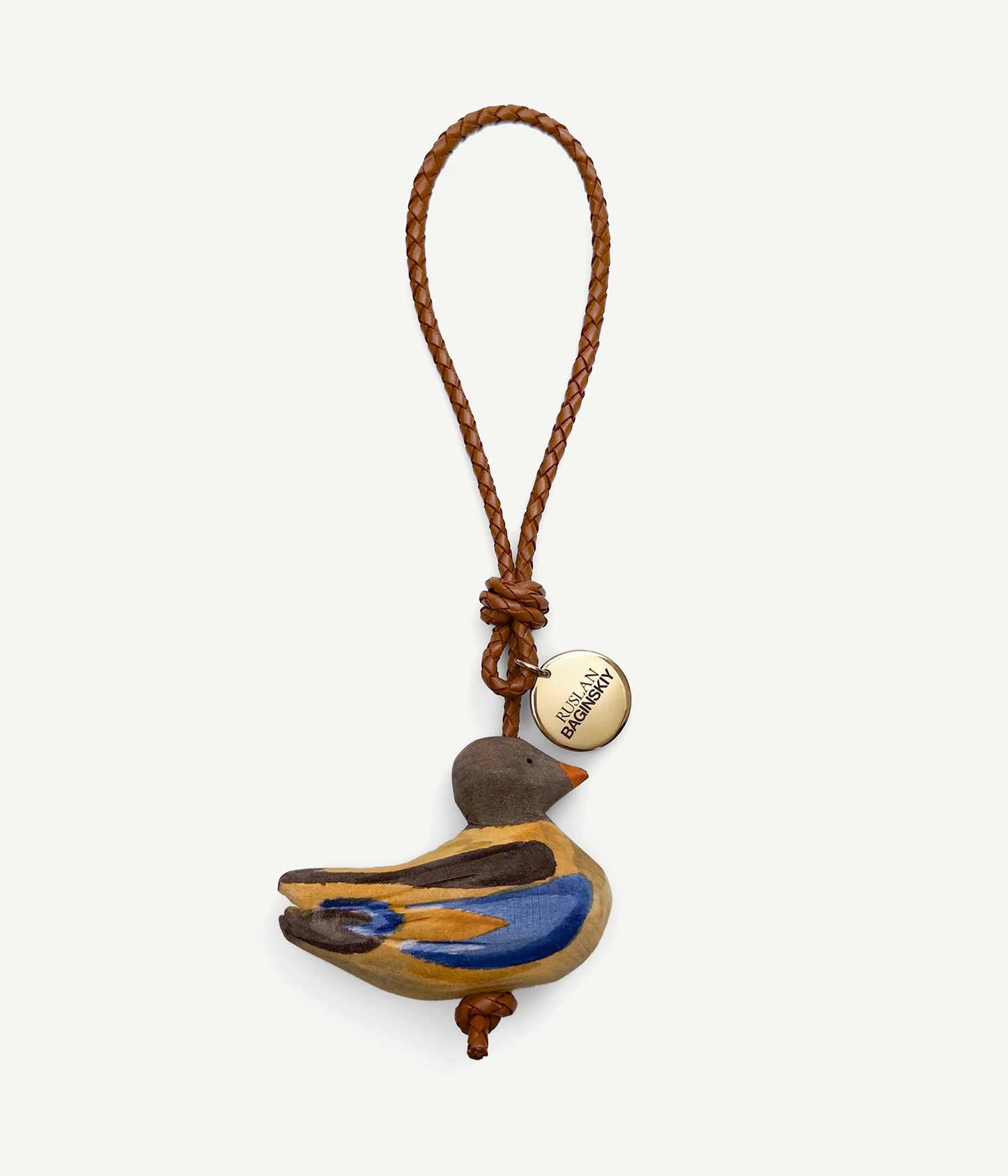 ALLwithoudDIS, RB Bag Charms embody deeply familiar symbols, each carries the emotional legacy of home. Each with its own character — a traveler or a guardian, a dreamer or a quiet observer. Hand-carved from natural wood, delicately painted each bag charm features a leather strap, and finished with an RB metal logo-medallion.The Ducks — finding peace along calm riverbanks, they symbolize inner calm and serenity. Ducks invite us to pause, to listen, and to reconnect with the stillness of nature.