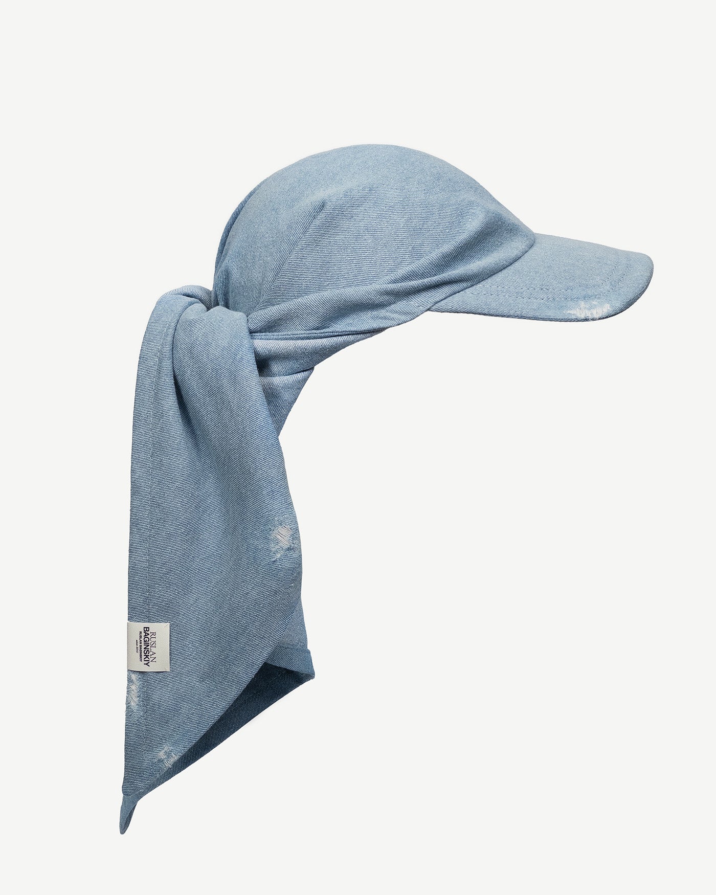 Hats, Ruslan Baginskiy Denim Scarf Visor A modern summer take on a headwear classic, this scarf with a visor is crafted from light blue denim. It can be tied at the back or left to drape freely over the shoulders. The asymmetrical shape adds dynamic flair and serves as a bold stylistic accent. Finished with an accent Ruslan Baginskiy logo.Handmade in Ukraine.